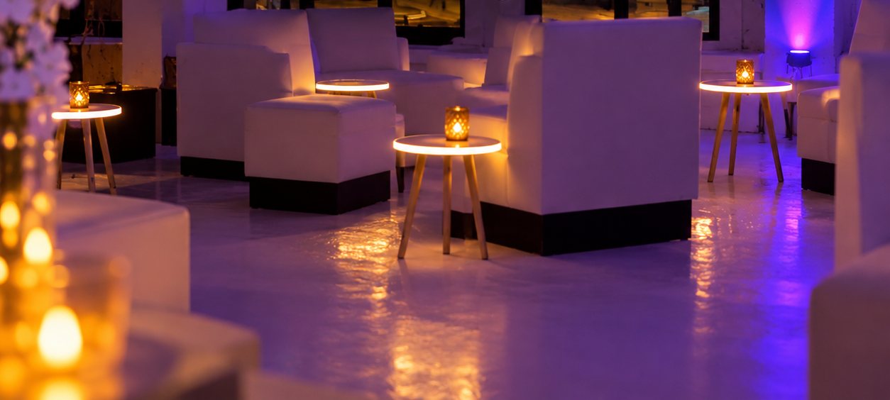 The Overlook lounge — white seating, candlelit tables and violet uplighting on a glossy floor